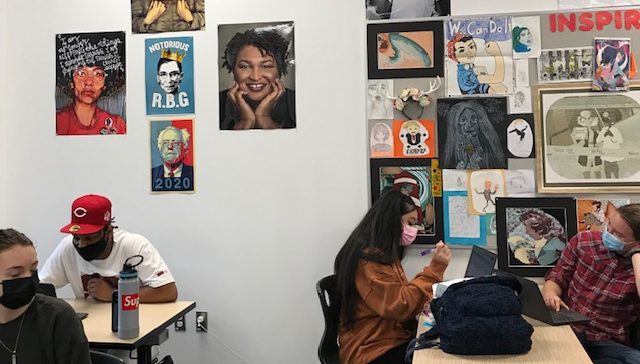 Students working on their current assignments. Behind them are posters and artworks that set the tone for the movements they’ll study.