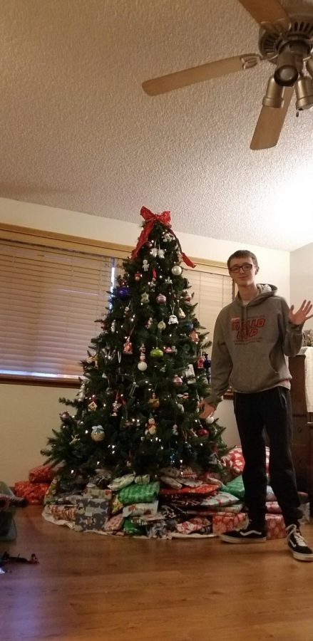 Reporter Calvin Lumadue standing next to gifts and the Christmas tree 