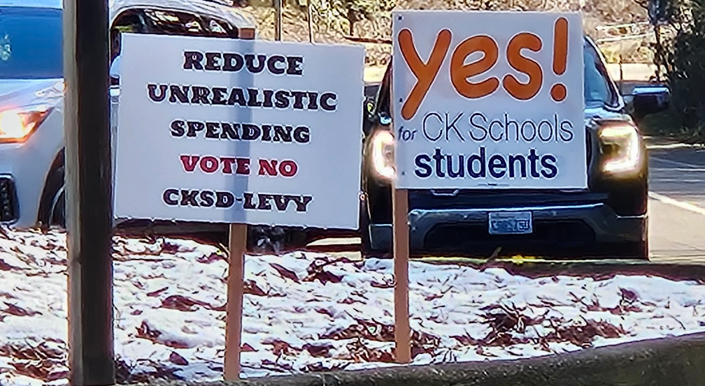 Signs advocating for and against the levy stand next to each other outside of Central Kitsap High School, the anti-levy sign identifying the levy tax as unrealistic spending while the pro-levy sign identifies the levy as a student resource.