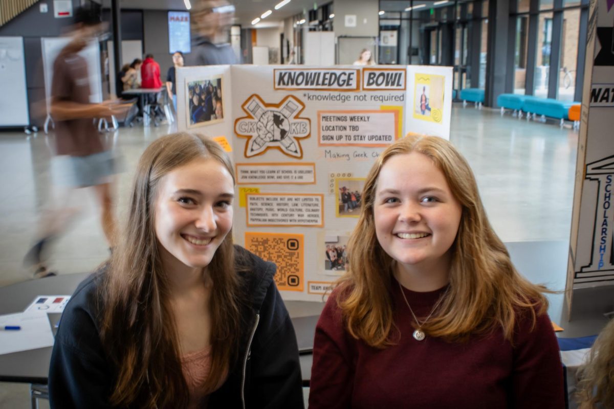 Olivia Jensen (left) and Audrey Holyoak (right) smiling for a photo in front of their club trifold