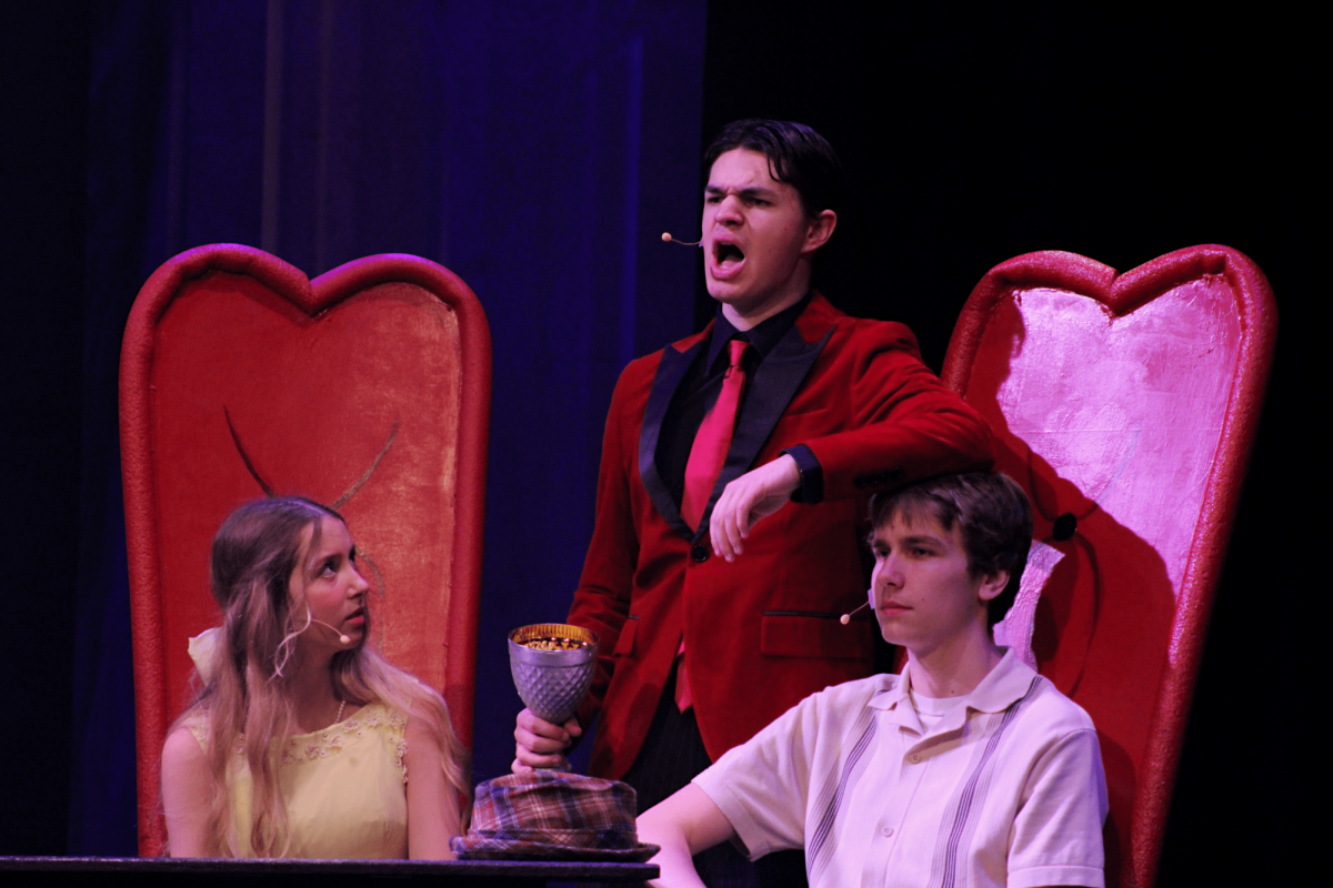 Gomez Addams (Miles Borer) uses Mal Beineke's (Maison Petersen) head as an armrest as Alice Beineke (Annabelle Havers) watches on.