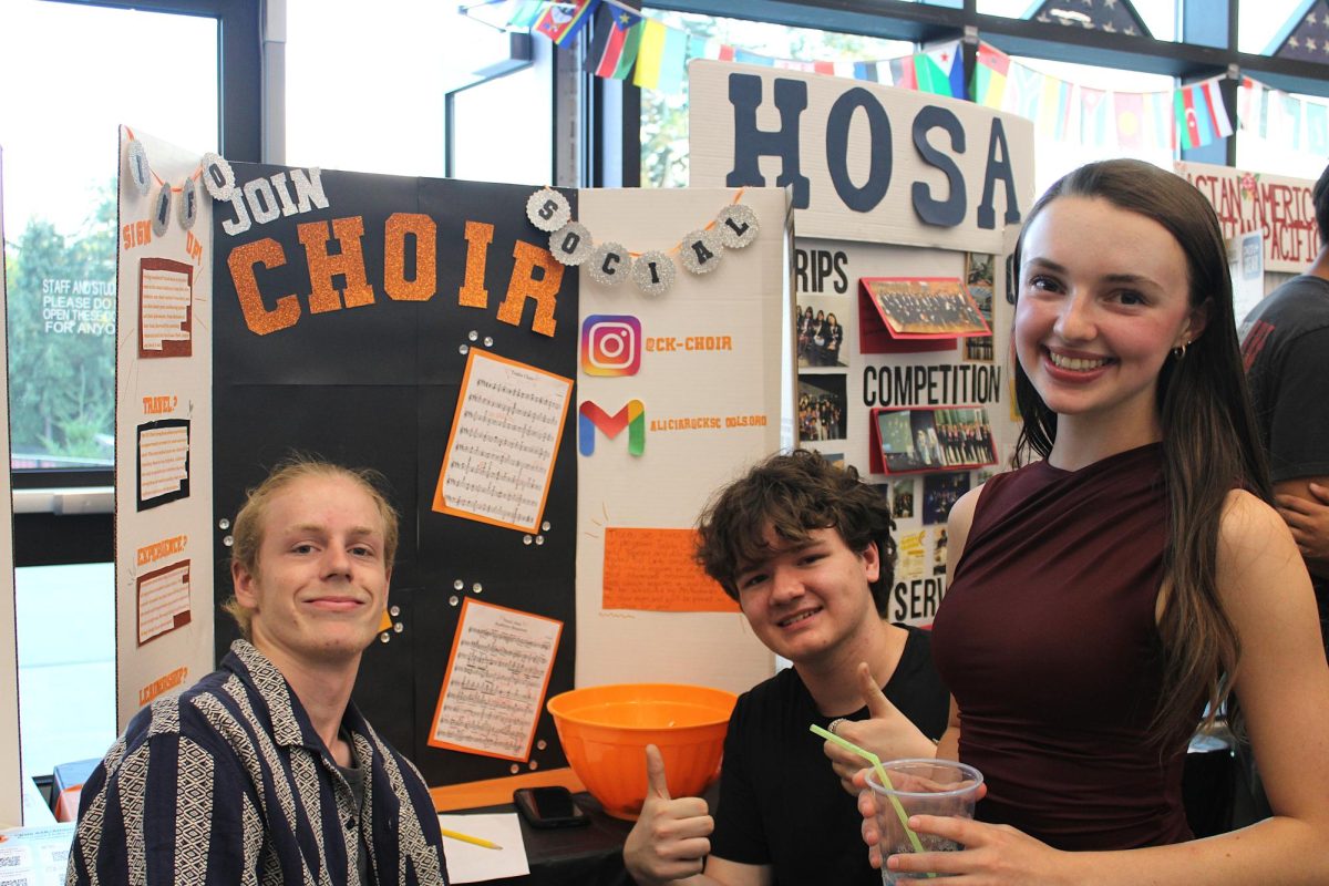 Clint Parker (left), Micah Boike (center), and Elliana Roberson (right) smile in front of the Choir trifold.