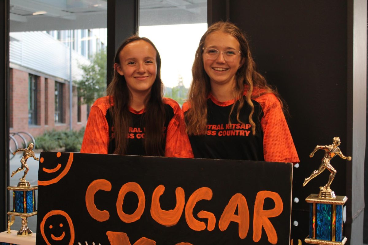 ‘Phoebe Tanori (left) and Stella Gartner (right) smile behind the cross country trifold.’