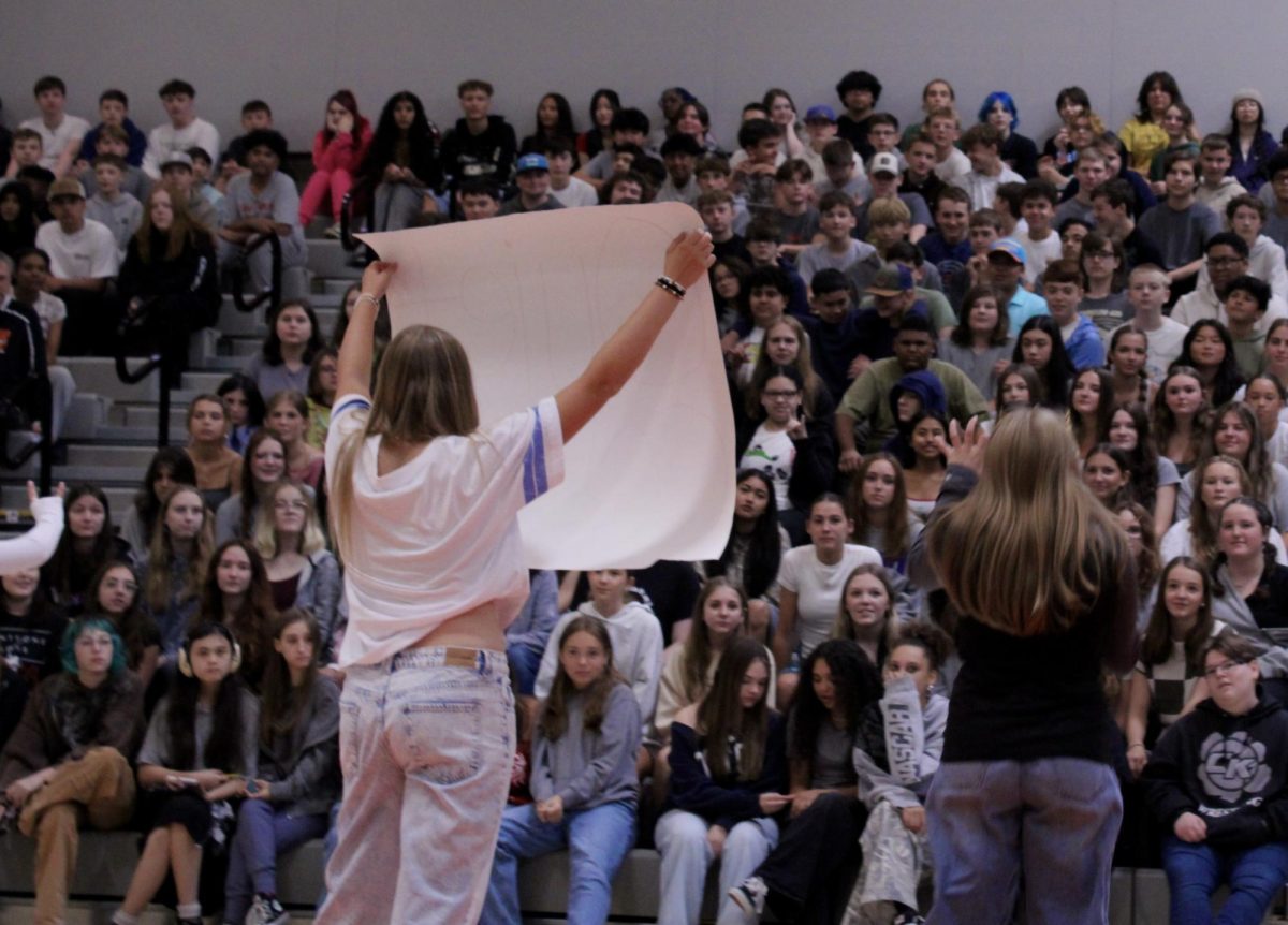 Lily Lay (left) and Ava Chadwick (right) tell the freshmen crowd to be quiet before holding up the "crazy cougar" sign. 