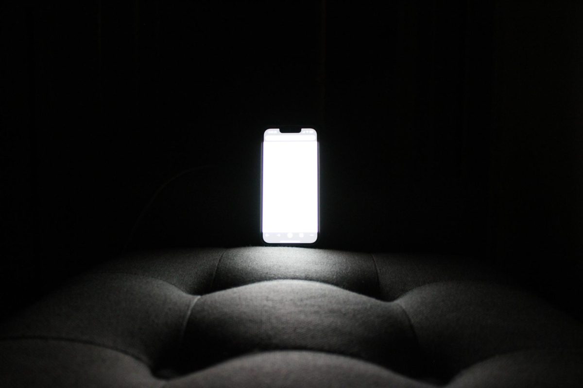 A phone glows surrounded by darkness demonstrating harm of blue light at night.