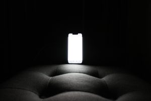 A phone glows surrounded by darkness demonstrating harm of blue light at night.