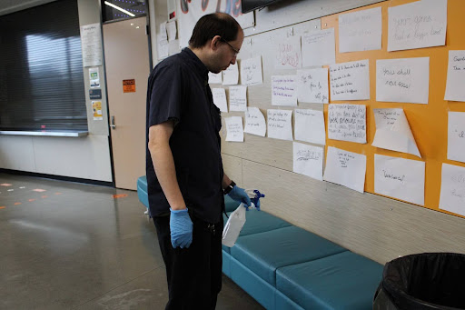 Day custodian Chris Pevovar sprays down a bench outside the Cougar Den during advisory.